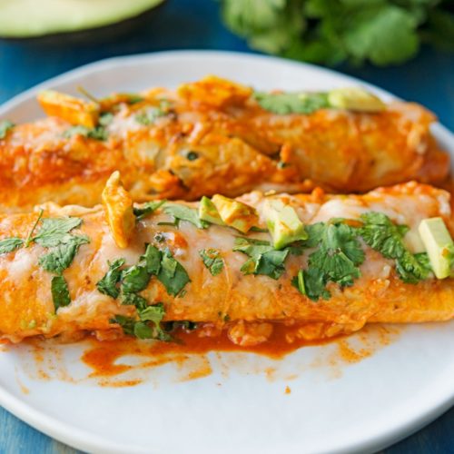 enchiladas with avocado and cilantro on a white plate